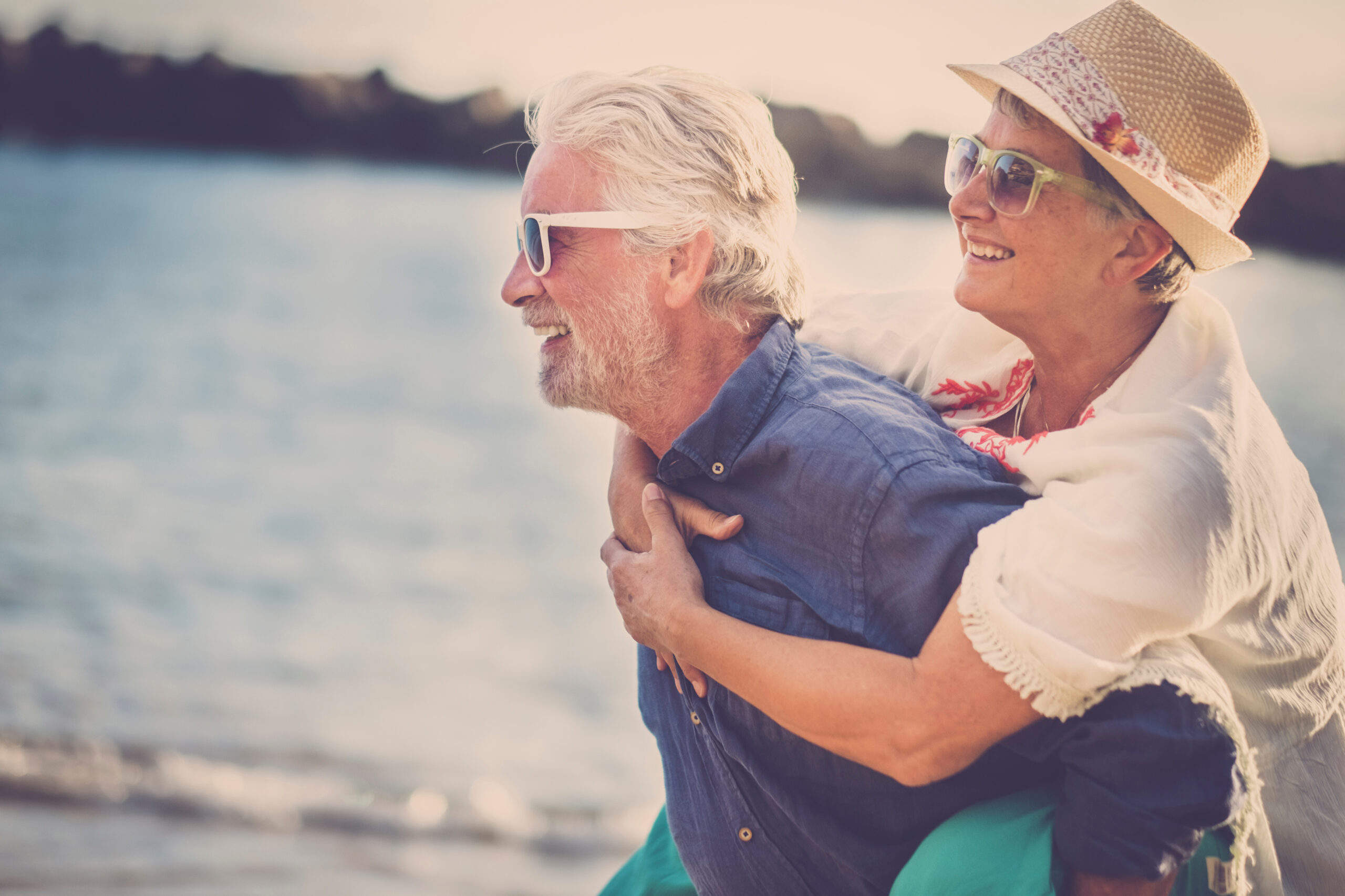 happy senior couple have fun and enjoy outdoor leisure activity at the beach. the man carry the woman on his back to enjoy together a retired lifestyle at the beach. smiling and laughing persons